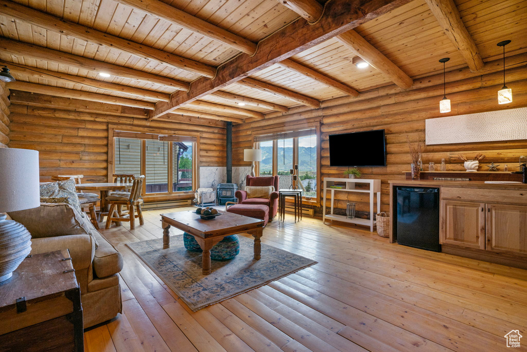 Living area featuring a wooden ceiling with exposed beams, a wood stove, rustic walls, and light wood finished floors