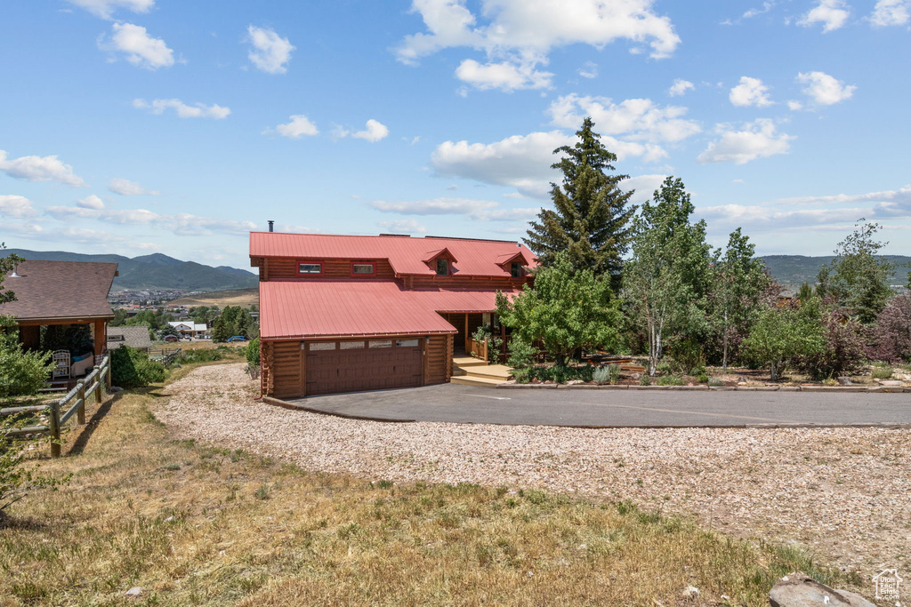 View of front of property featuring a mountain view, asphalt driveway, a metal roof, and a garage
