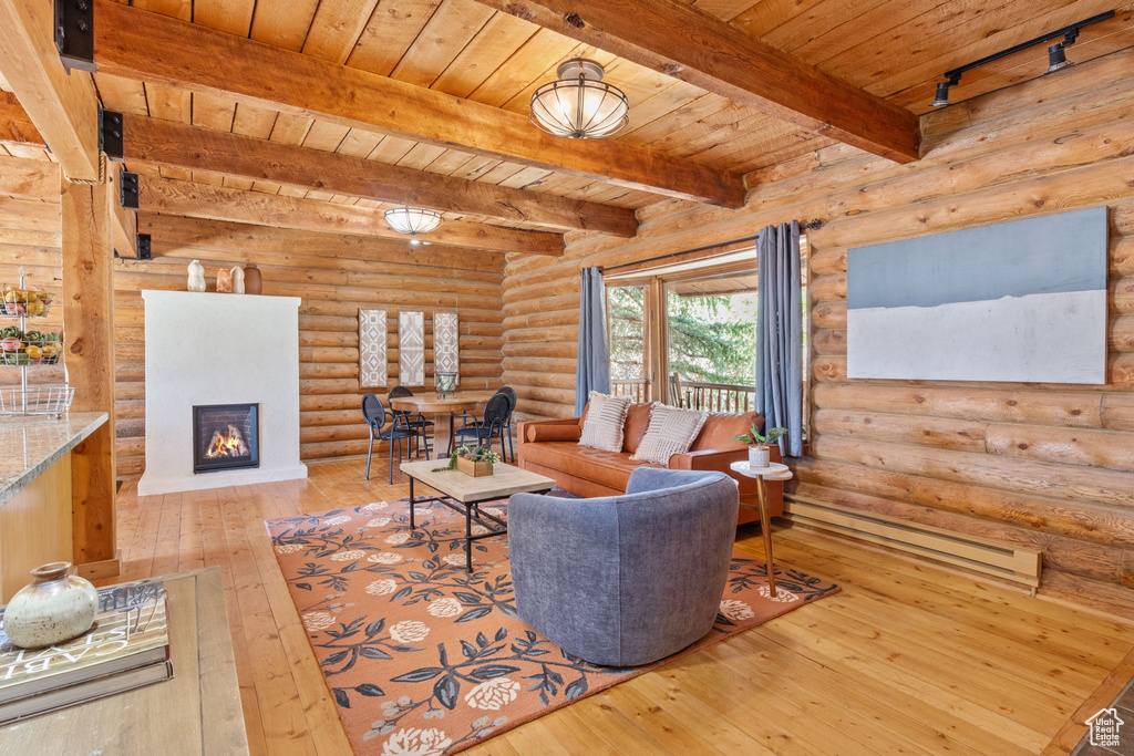 Living room with wood-type flooring, a baseboard heating unit, a wooden ceiling with exposed beams, a lit fireplace, and rustic walls