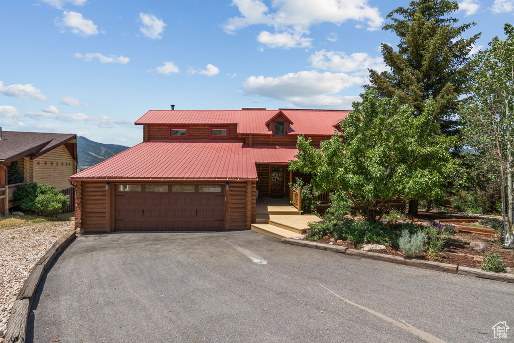 Cabin featuring log exterior, driveway, a metal roof, and a garage