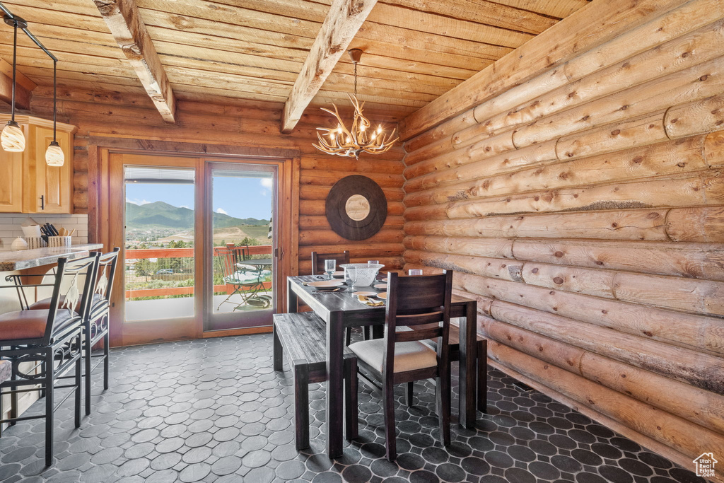 Dining room with a wooden ceiling with exposed beams, a chandelier, and rustic walls