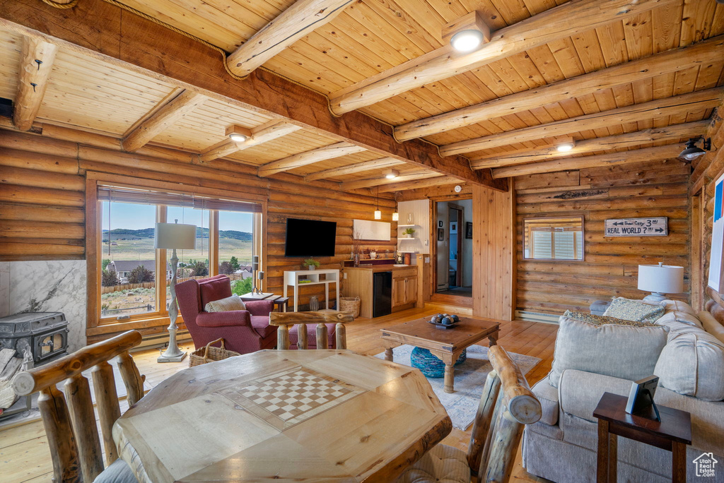 Dining room featuring a wood ceiling with exposed beams, light wood-style floors, log walls, and a wood stove