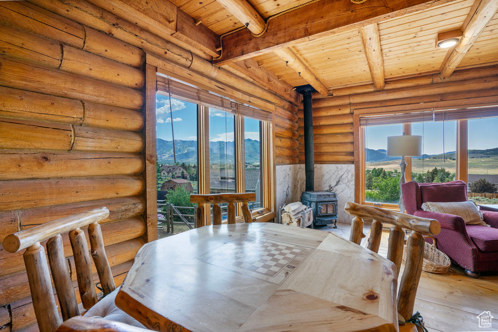 Dining space featuring a wood ceiling with exposed beams, hardwood / wood-style floors, a mountain view, a wood stove, and log walls