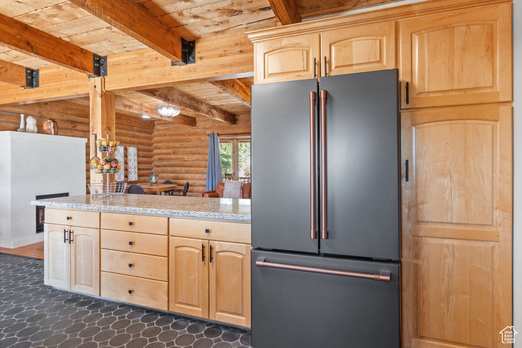 Kitchen with high end fridge, rustic walls, light brown cabinetry, a wooden ceiling with exposed beams, and light stone counters