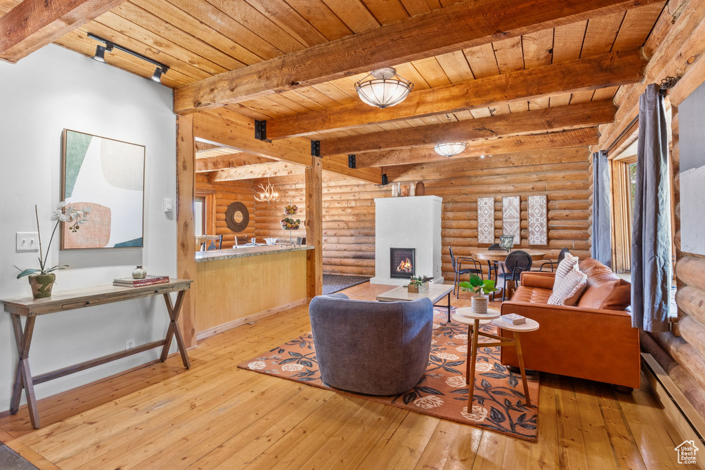 Living area featuring baseboard heating, a wooden ceiling with exposed beams, hardwood / wood-style flooring, a lit fireplace, and rustic walls