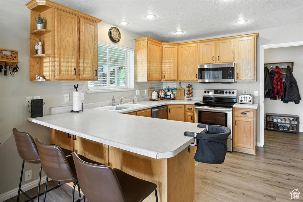 Kitchen with stainless steel appliances, a peninsula, light countertops, light wood-type flooring, and a kitchen bar