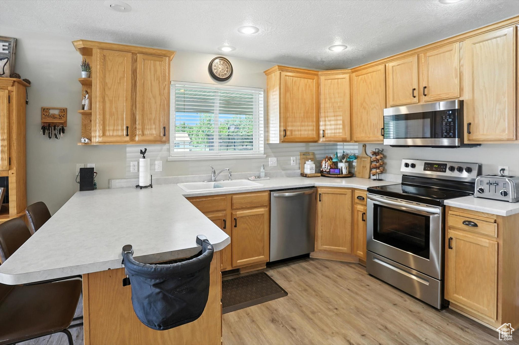 Kitchen with stainless steel appliances, a peninsula, a breakfast bar, light countertops, and light wood finished floors