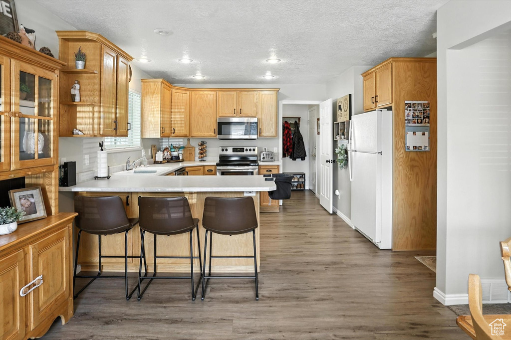 Kitchen with appliances with stainless steel finishes, a peninsula, light countertops, dark wood-style floors, and a kitchen breakfast bar