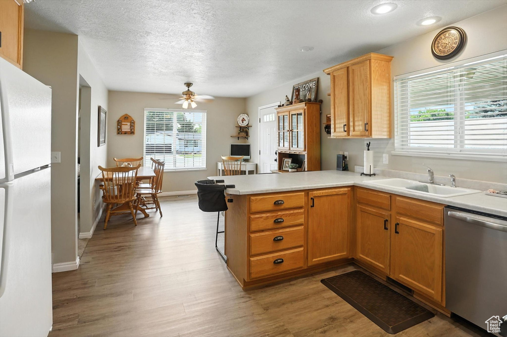 Kitchen featuring freestanding refrigerator, stainless steel dishwasher, a peninsula, light wood-type flooring, and a textured ceiling