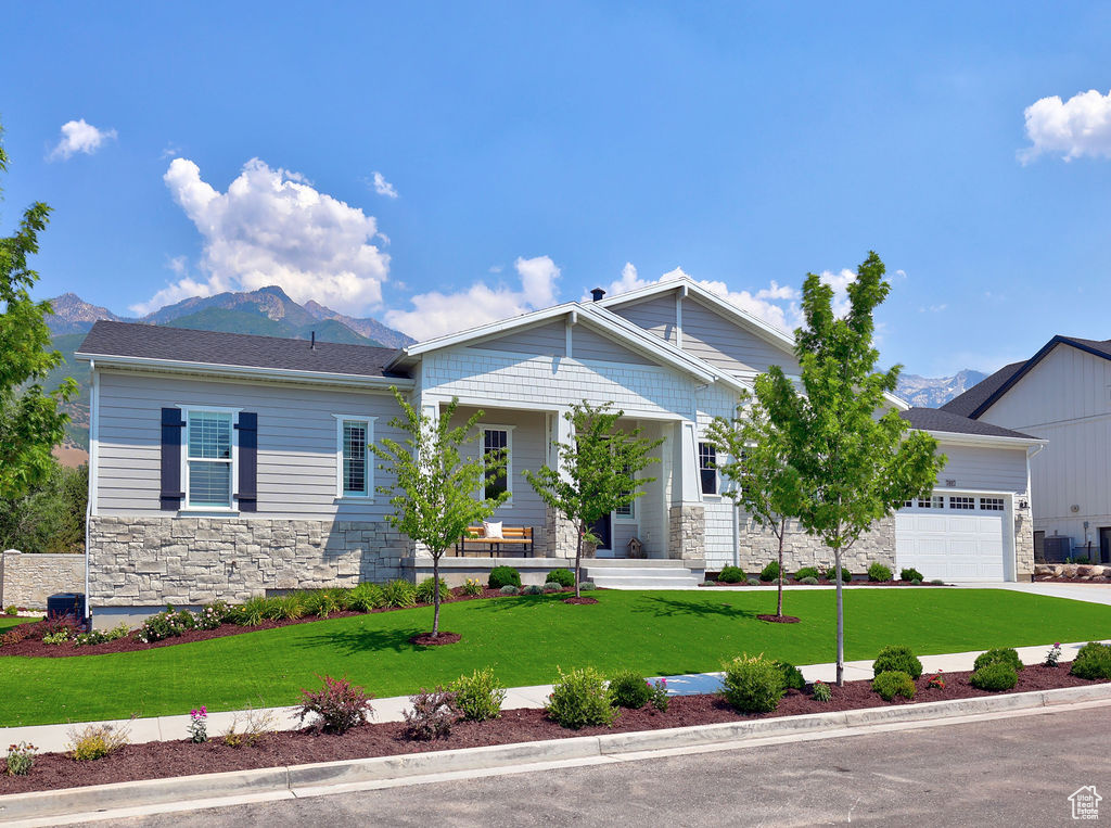 View of front of property with stone siding, a mountain view, covered porch, and a front lawn