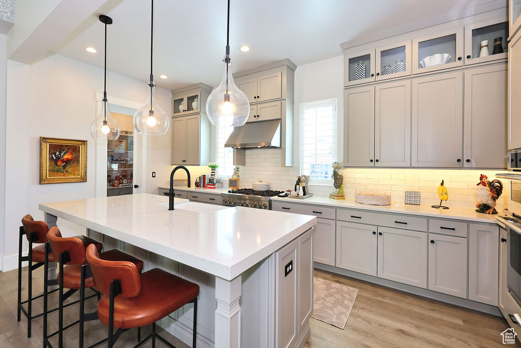 Kitchen with under cabinet range hood, backsplash, an island with sink, a breakfast bar, and light countertops