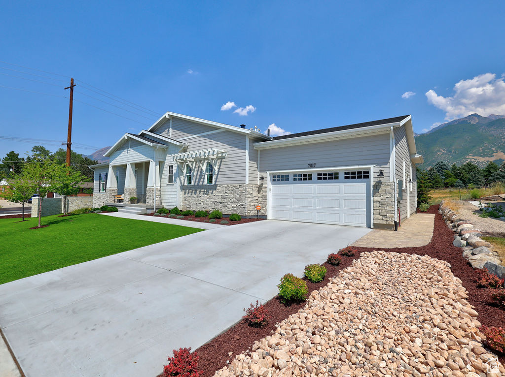 View of front of home featuring an attached garage, concrete driveway, stone siding, a front lawn, and a mountain view