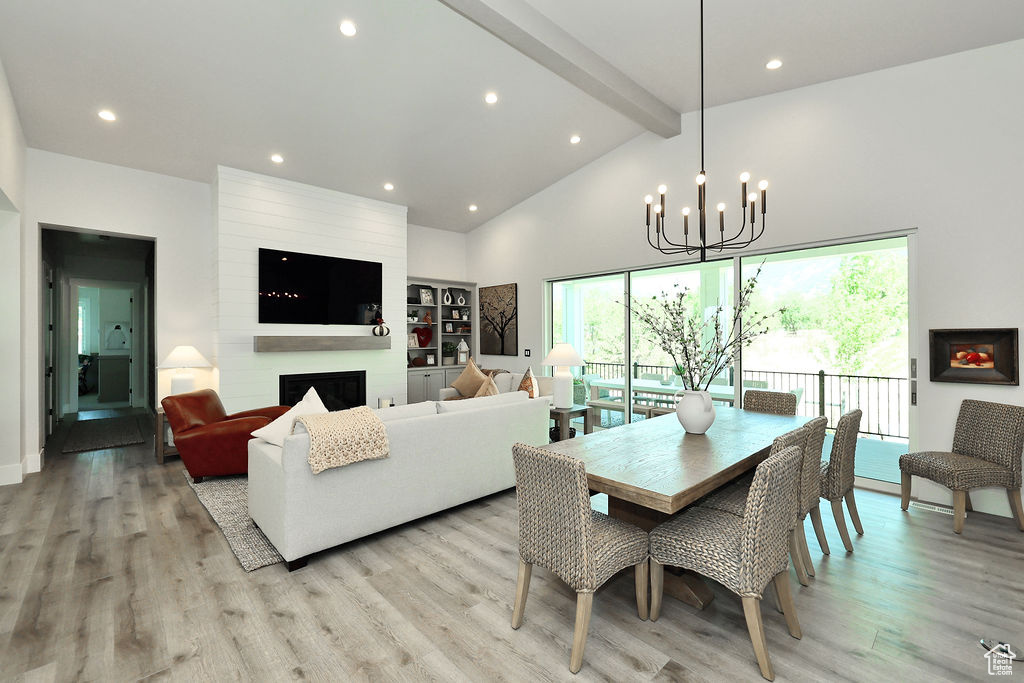 Dining space featuring beam ceiling, a chandelier, light wood-style flooring, high vaulted ceiling, and a large fireplace