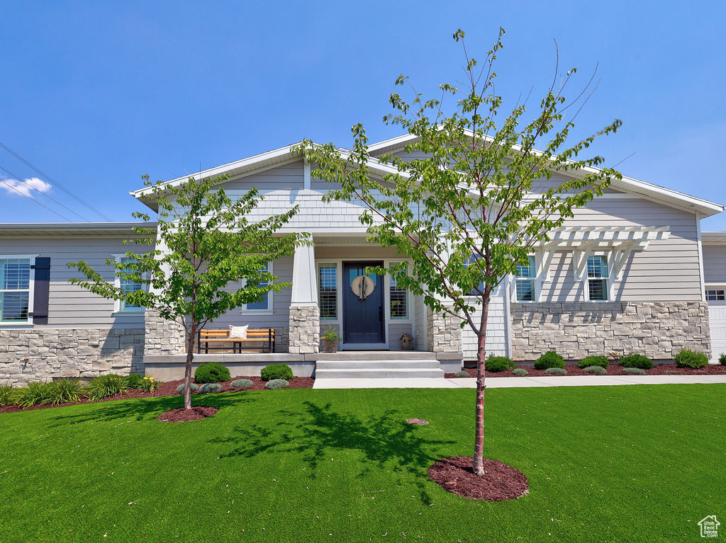 Craftsman-style home with stone siding, a front lawn, covered porch, and a pergola