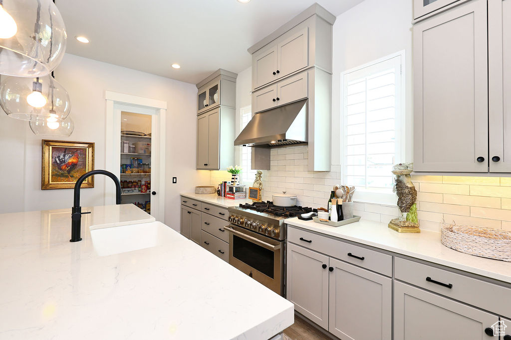 Kitchen featuring high end range, under cabinet range hood, gray cabinets, backsplash, and recessed lighting