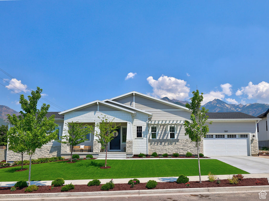 View of front facade featuring stone siding, a mountain view, an attached garage, a front lawn, and concrete driveway