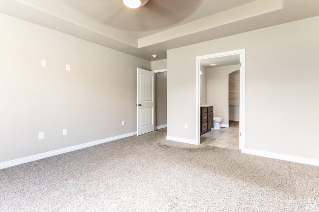 Unfurnished bedroom featuring light colored carpet, ensuite bathroom, and arched walkways
