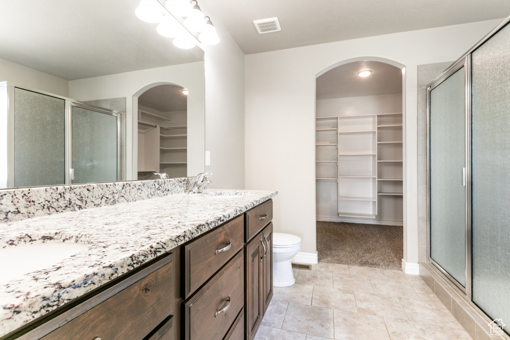 Bathroom with a walk in closet, double vanity, a shower stall, and tile patterned floors