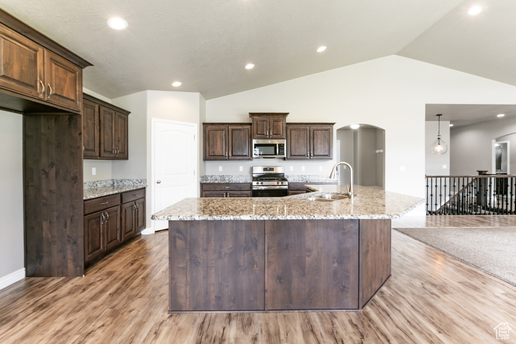 Kitchen featuring stainless steel appliances, arched walkways, light wood-style flooring, lofted ceiling, and dark brown cabinets