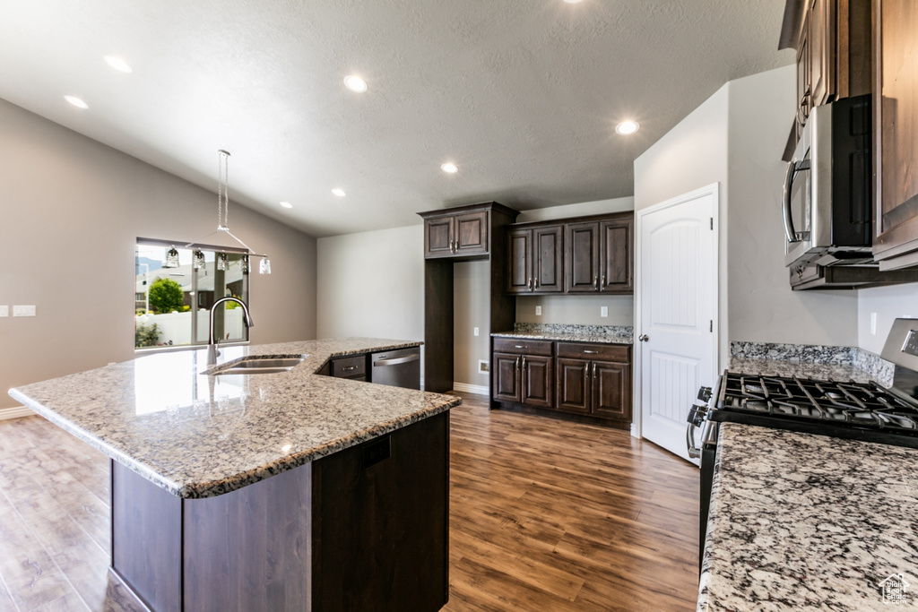 Kitchen featuring stainless steel appliances, dark wood-style flooring, vaulted ceiling, a kitchen island with sink, and dark brown cabinetry