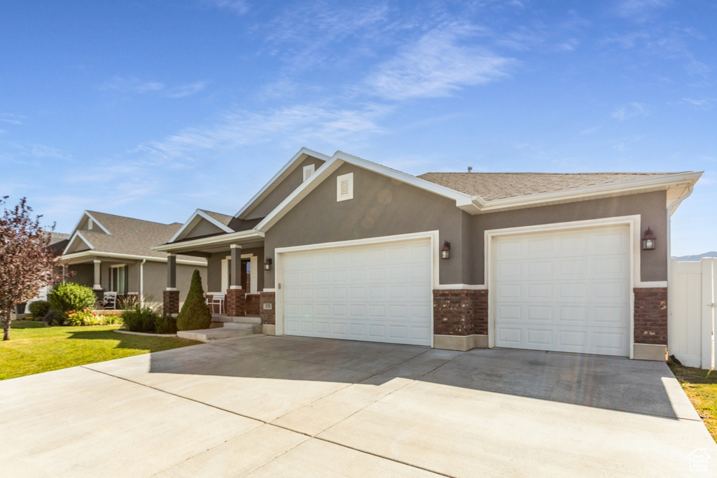 View of front of house featuring an attached garage, driveway, brick siding, and stucco siding