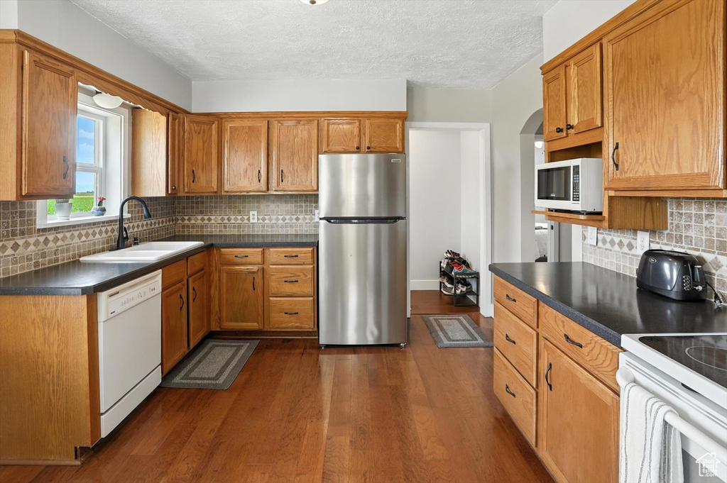 Kitchen featuring white appliances, dark countertops, dark wood finished floors, a textured ceiling, and decorative backsplash