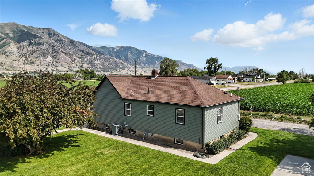 Back of house with a chimney, a lawn, a mountain view, and roof with shingles