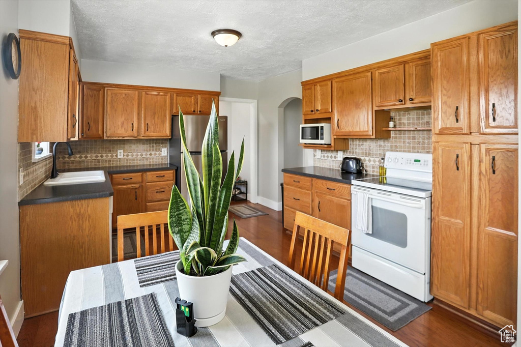 Kitchen with white appliances, arched walkways, tasteful backsplash, dark countertops, and brown cabinetry