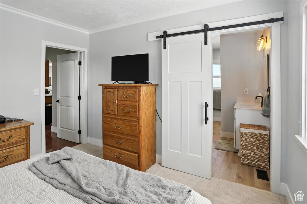 Bedroom featuring a barn door, ornamental molding, and wood finished floors