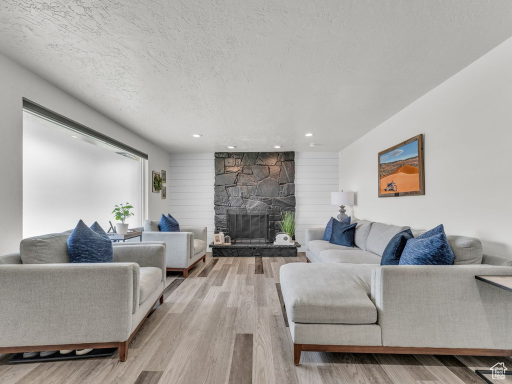 Living area featuring light wood-style flooring, a textured ceiling, a fireplace, and recessed lighting