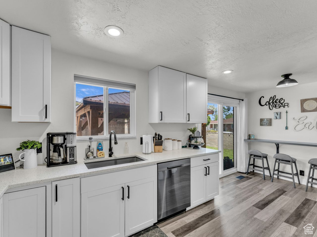 Kitchen featuring stainless steel dishwasher, a textured ceiling, white cabinets, light wood-style flooring, and recessed lighting