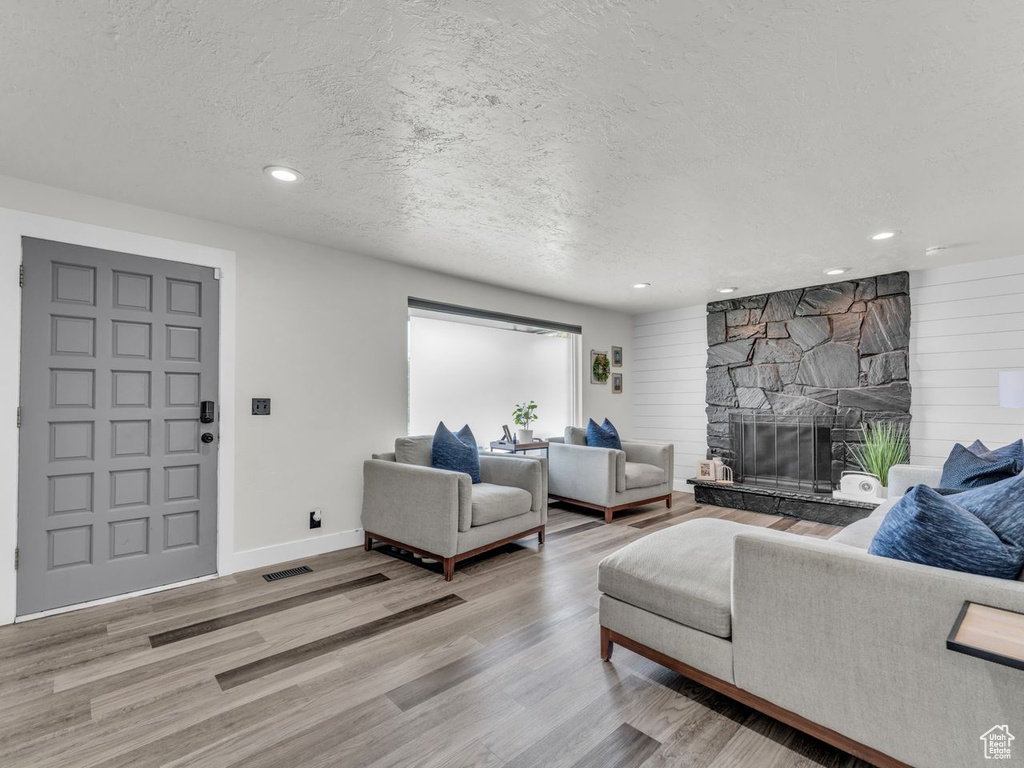 Living area with wood finished floors, a textured ceiling, recessed lighting, and a stone fireplace