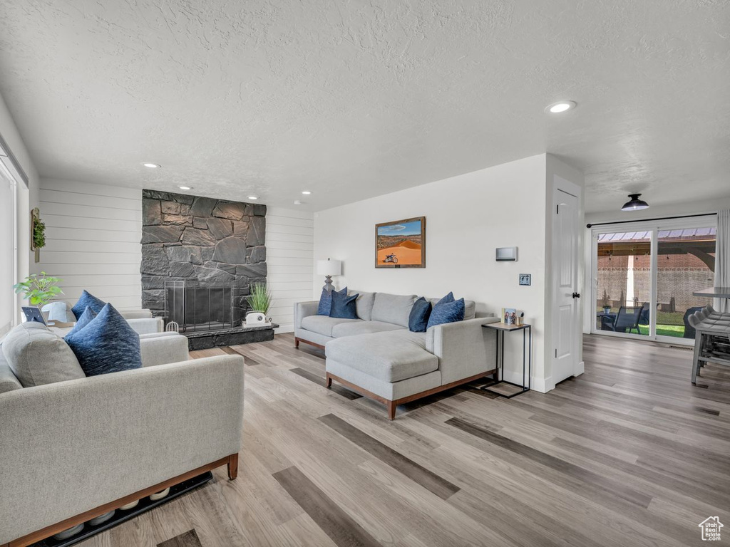 Living room featuring a textured ceiling, light wood-type flooring, recessed lighting, and a fireplace