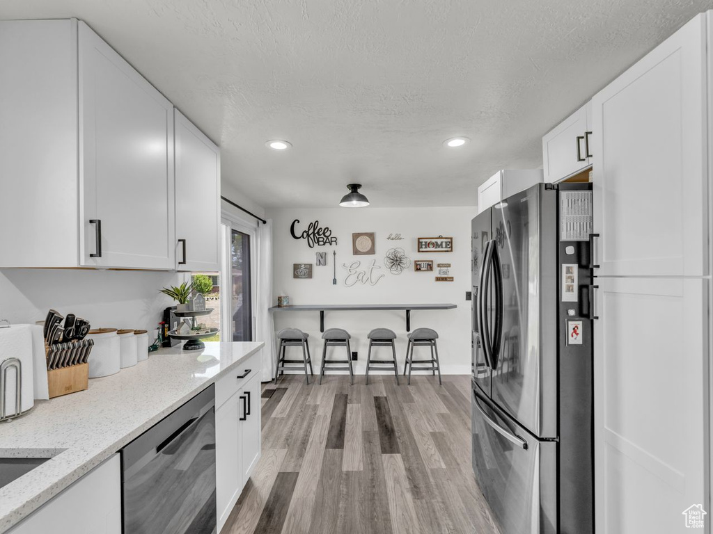 Kitchen with stainless steel appliances, white cabinets, wood finished floors, recessed lighting, and a textured ceiling