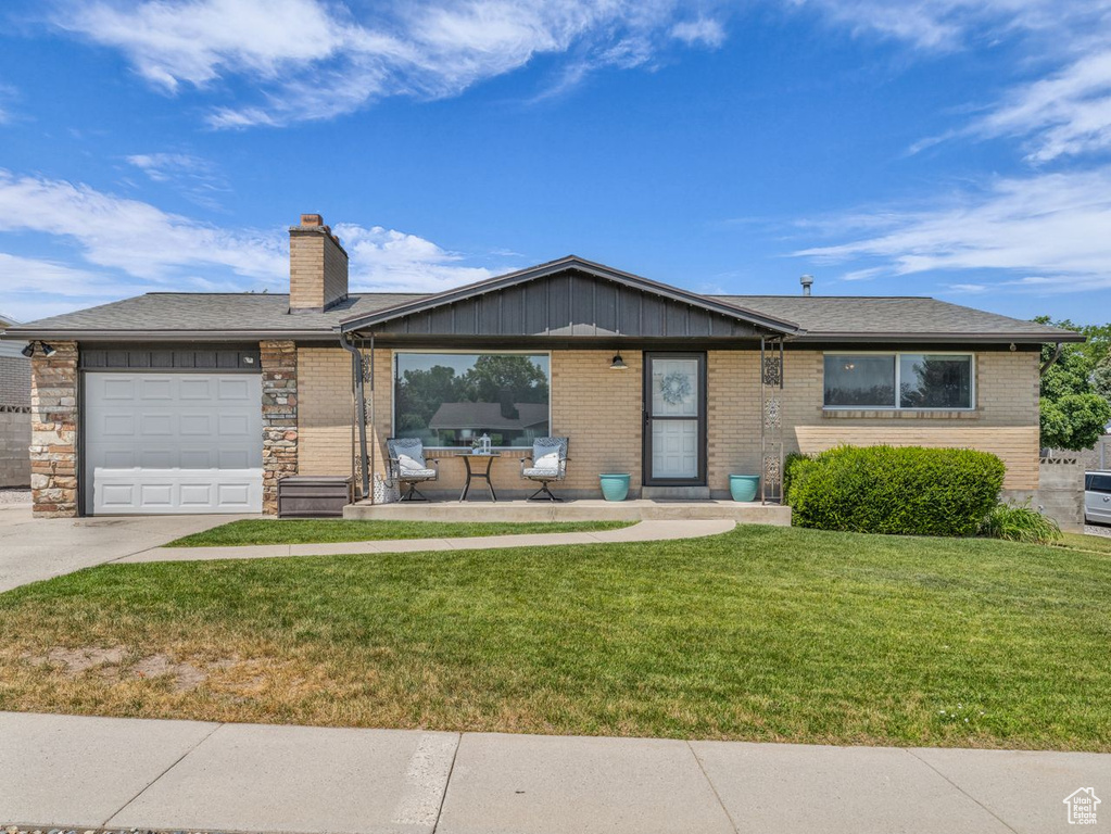 Ranch-style home with concrete driveway, an attached garage, a front yard, brick siding, and a chimney
