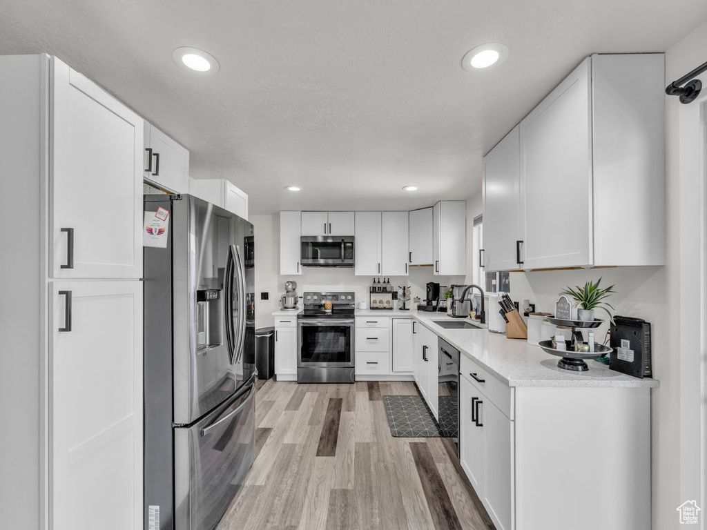 Kitchen featuring stainless steel appliances, light wood-style flooring, white cabinets, and recessed lighting