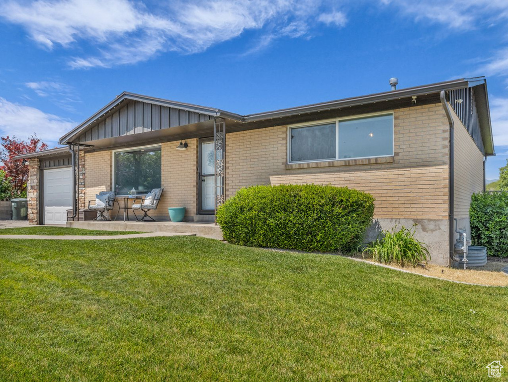 Ranch-style home featuring board and batten siding, an attached garage, brick siding, and a front yard