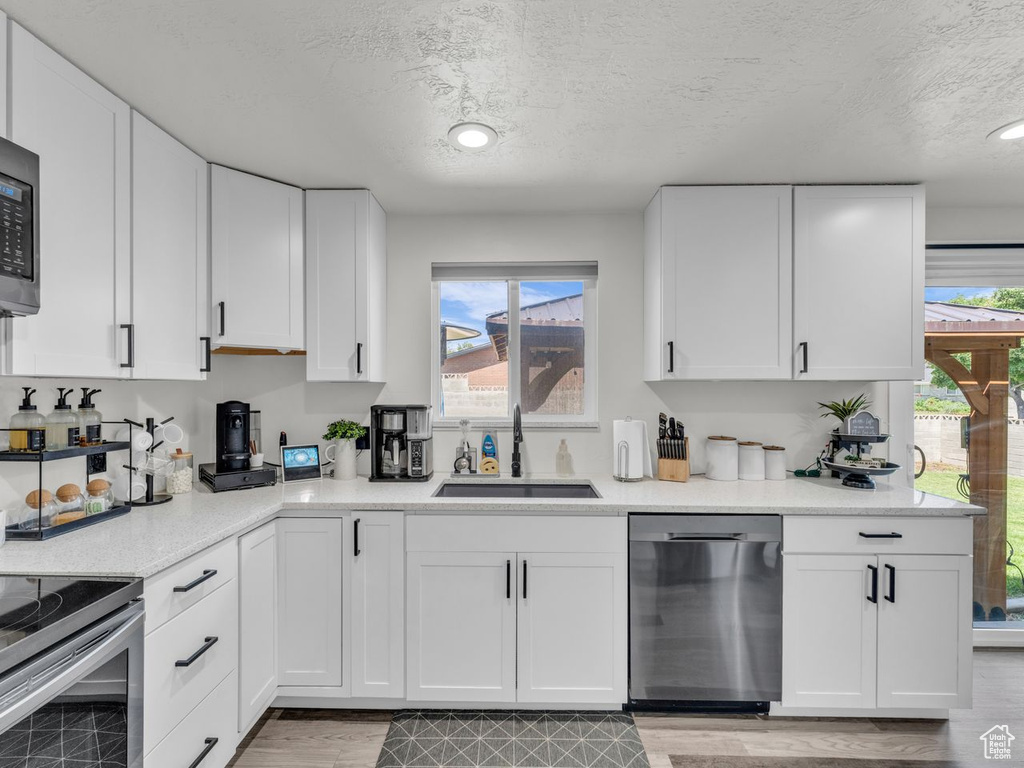 Kitchen featuring stainless steel dishwasher, a textured ceiling, white cabinets, light wood-style floors, and recessed lighting