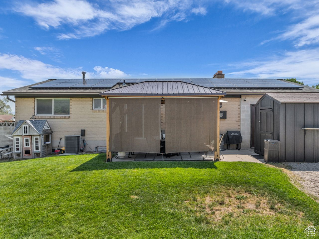 Back of property featuring a shed, roof mounted solar panels, brick siding, and a yard