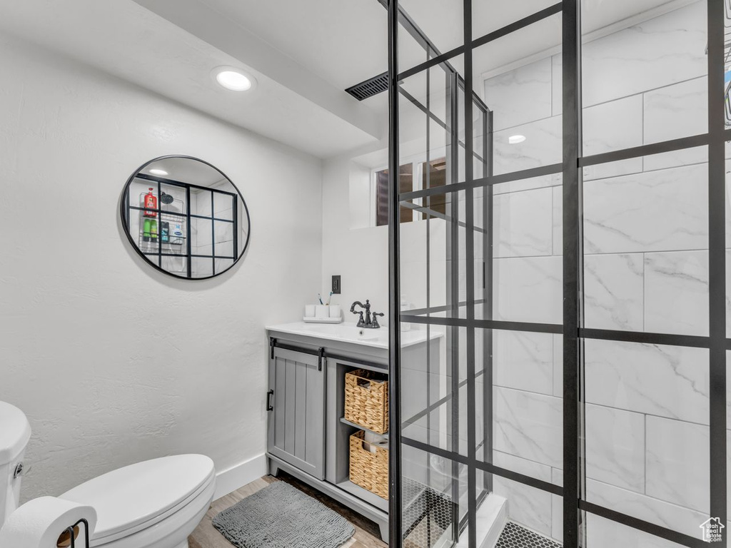 Bathroom featuring tiled shower, wood finished floors, vanity, and recessed lighting