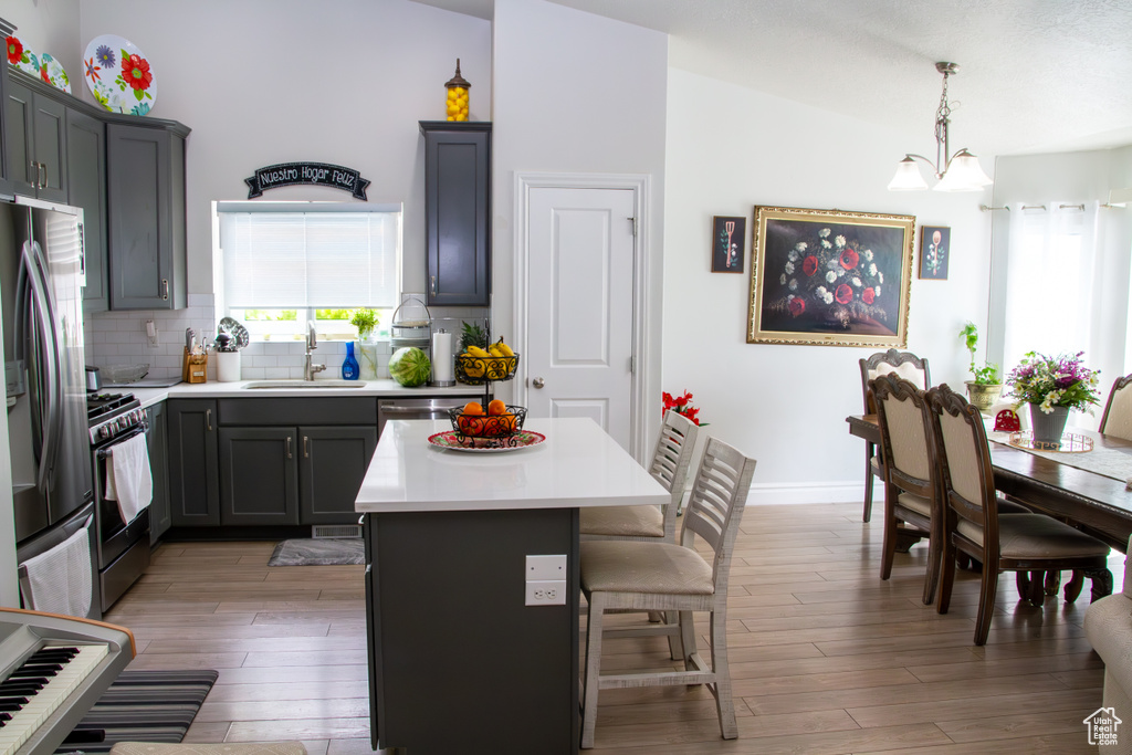 Kitchen with stainless steel appliances, light wood-type flooring, a kitchen bar, backsplash, and light countertops