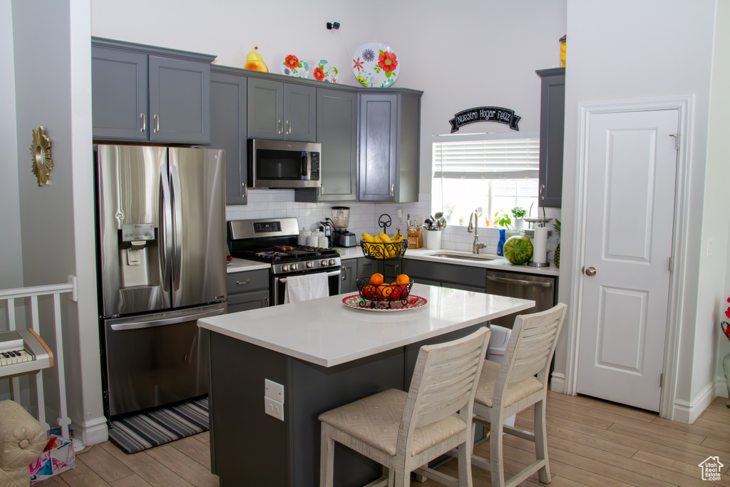 Kitchen with appliances with stainless steel finishes, light wood finished floors, decorative backsplash, a breakfast bar area, and light countertops