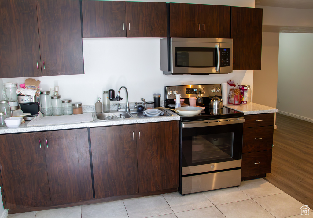 Kitchen with stainless steel appliances, dark brown cabinets, and light tile patterned flooring
