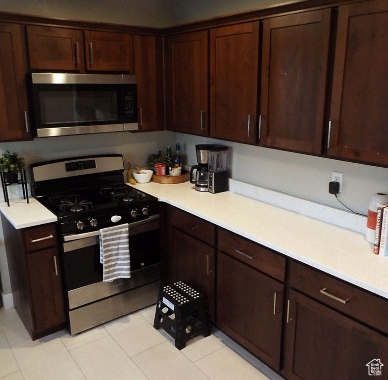Kitchen featuring stainless steel appliances, light countertops, light tile patterned floors, and dark brown cabinets
