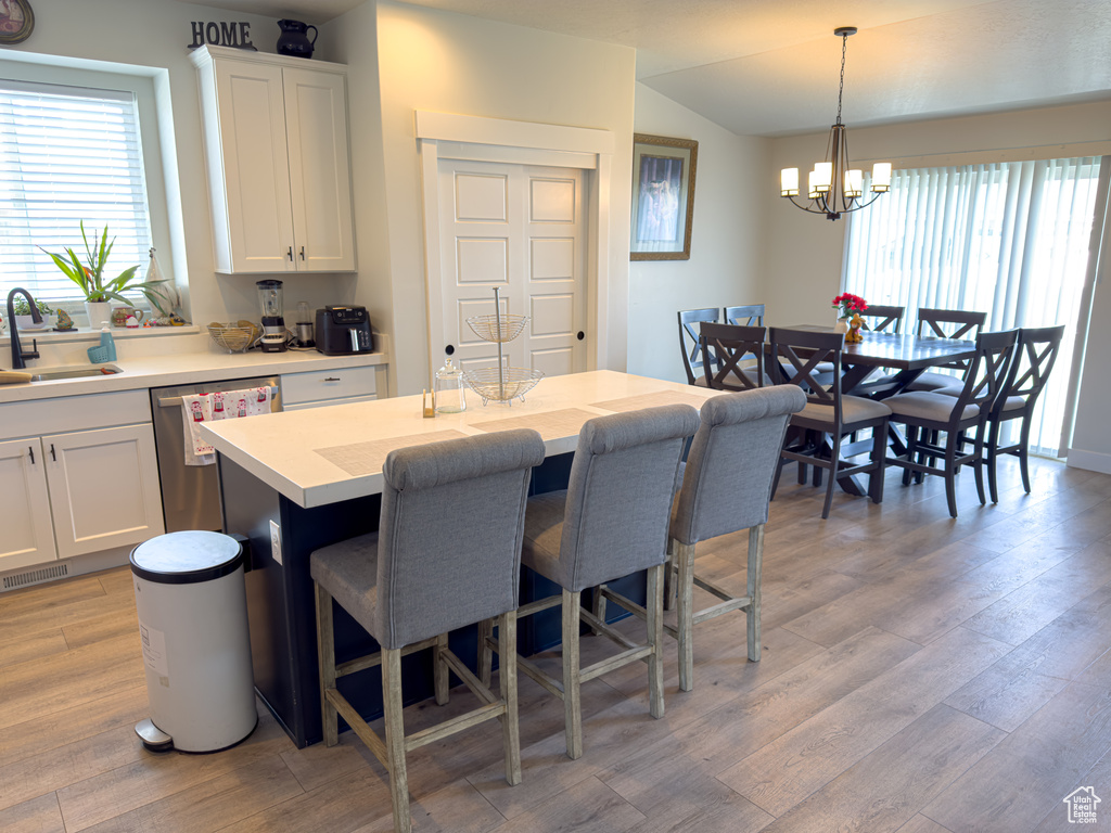 Kitchen with dishwasher, a breakfast bar, a chandelier, light wood-type flooring, and white cabinets