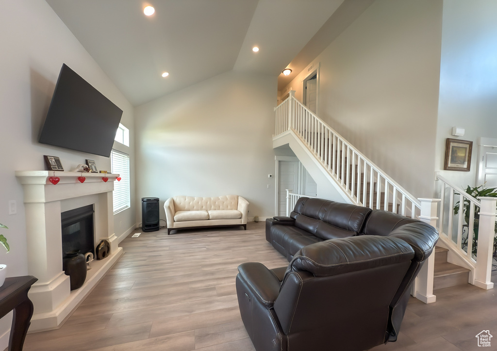 Living room featuring wood finished floors, a glass covered fireplace, stairs, lofted ceiling, and recessed lighting