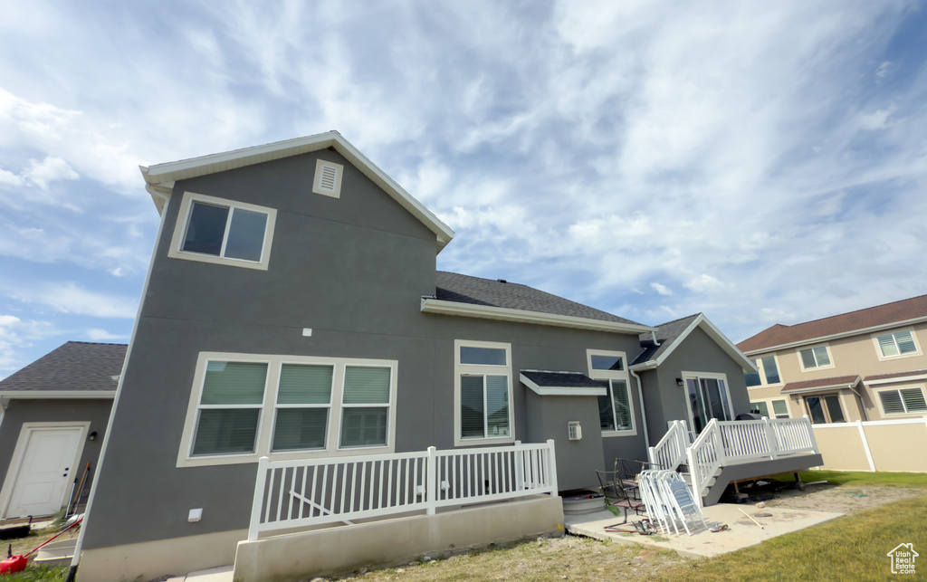 Rear view of property with a deck, stucco siding, roof with shingles, and a patio area