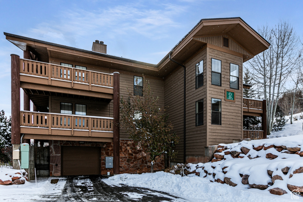 View of front of home with a balcony, a chimney, an attached garage, and stone siding