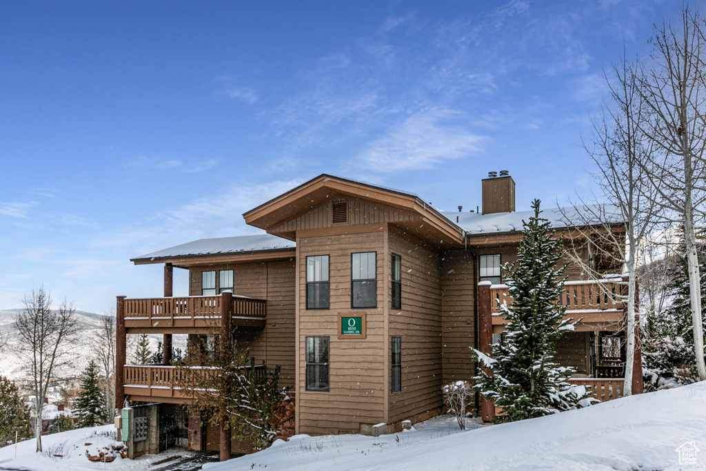 View of snowy exterior featuring a balcony and a chimney