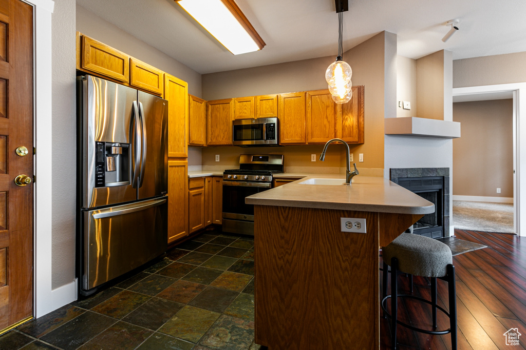 Kitchen with appliances with stainless steel finishes, a peninsula, light countertops, a kitchen bar, and hanging light fixtures